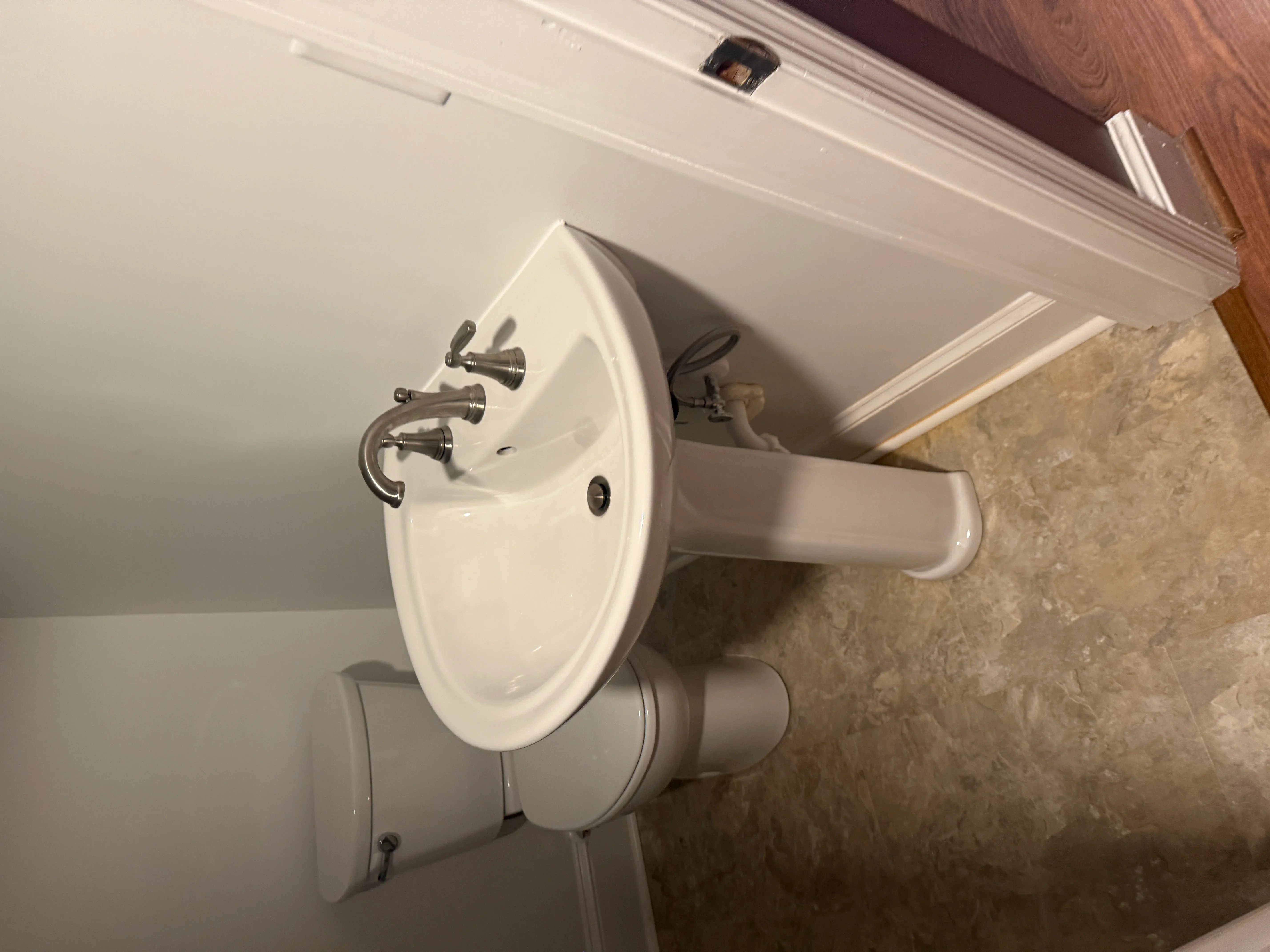 White ceramic pedestal sink with chrome faucet and supply lines installed against tile wall