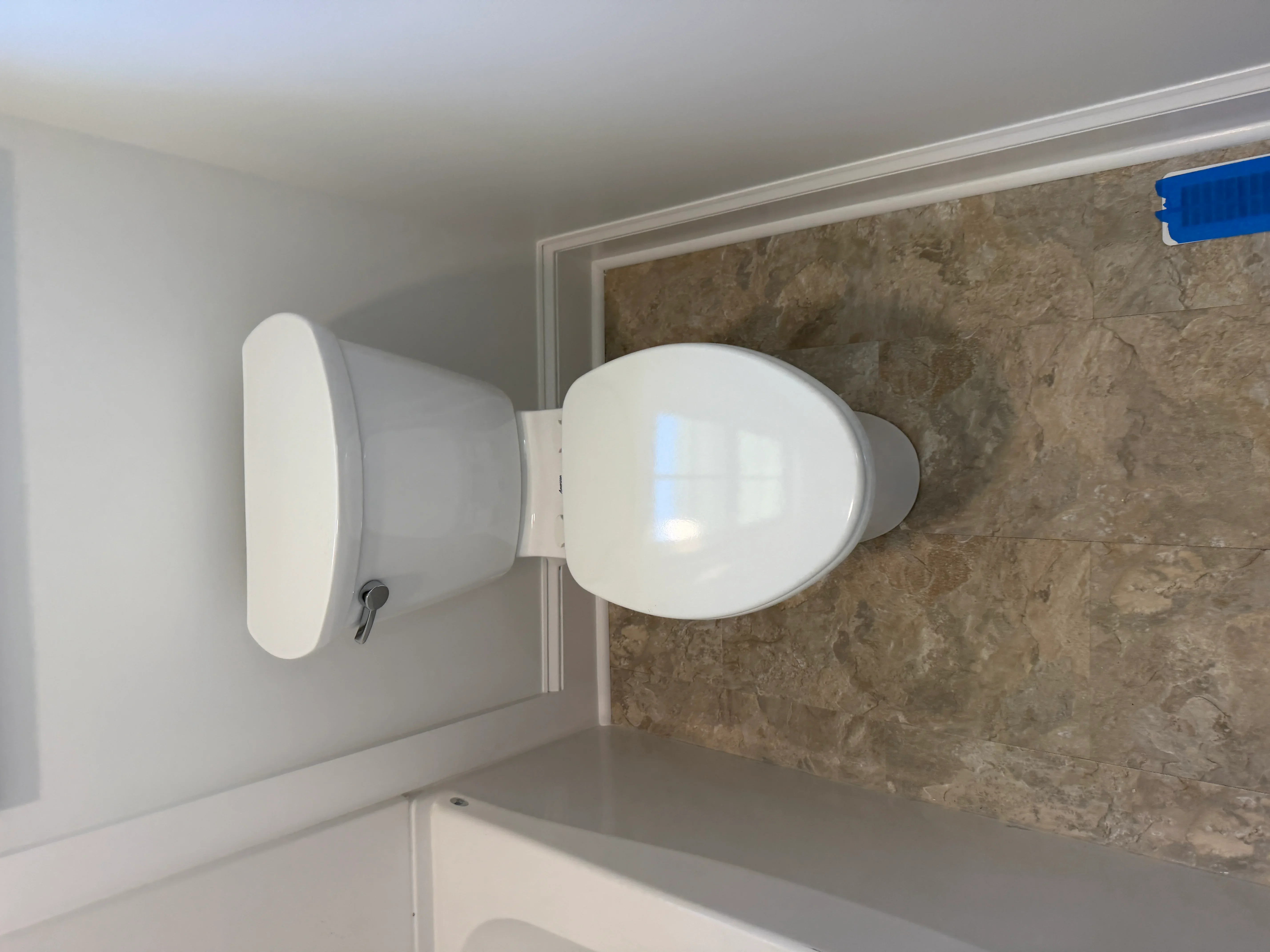 White two-piece toilet installed against stone tile wall with drywall and trim