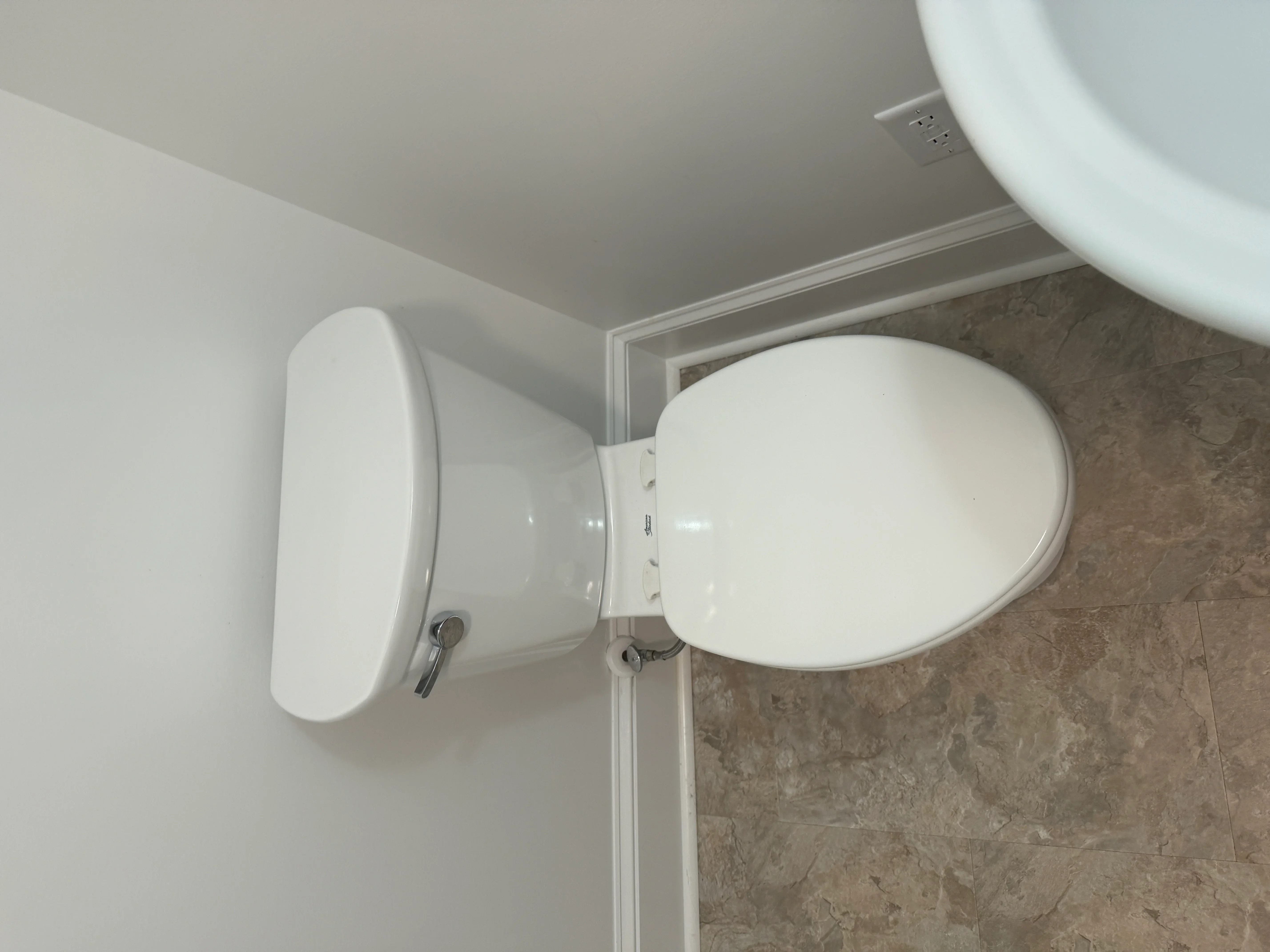 White ceramic toilet with soft-close seat installed on gray tile bathroom floor