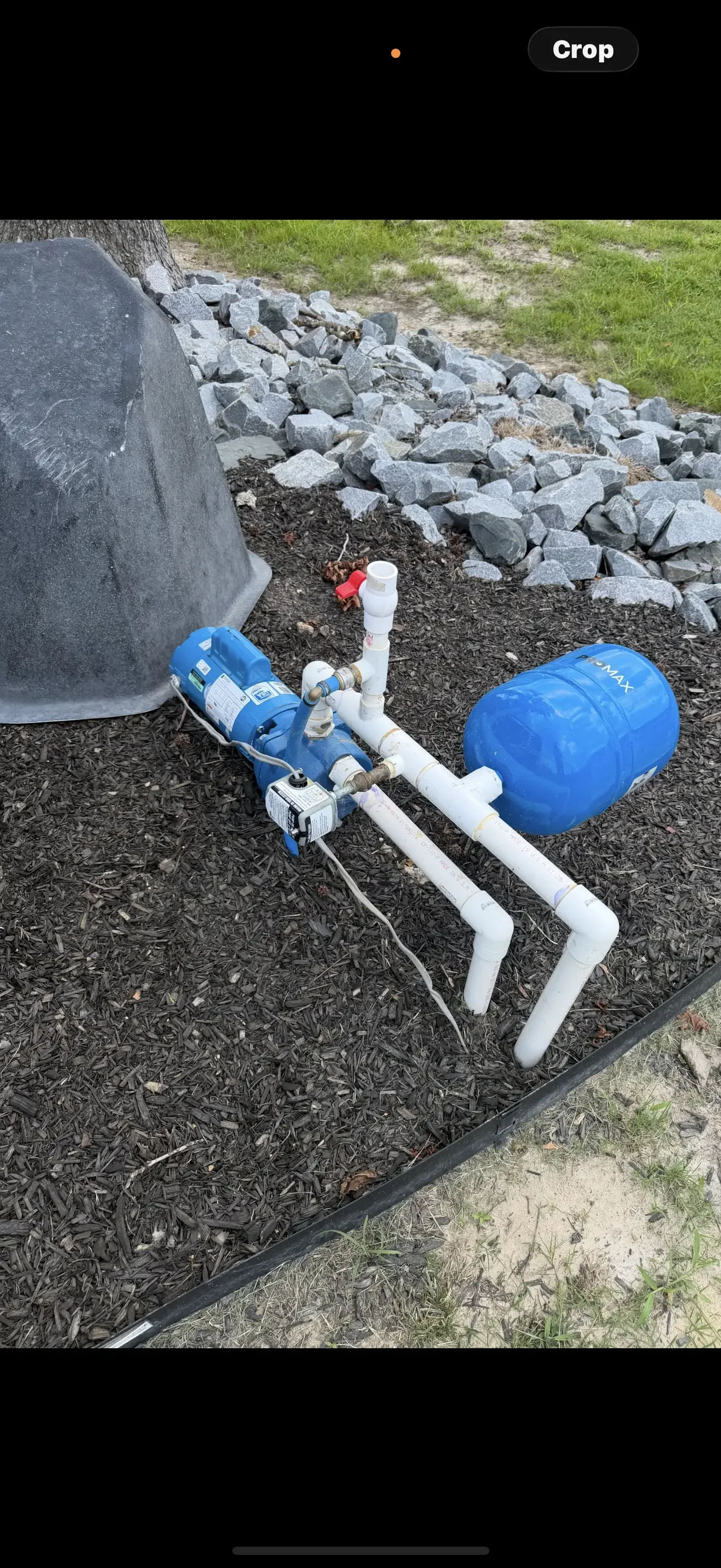 Blue pressure tank and submersible pump with white PVC piping and stone drainage installation
