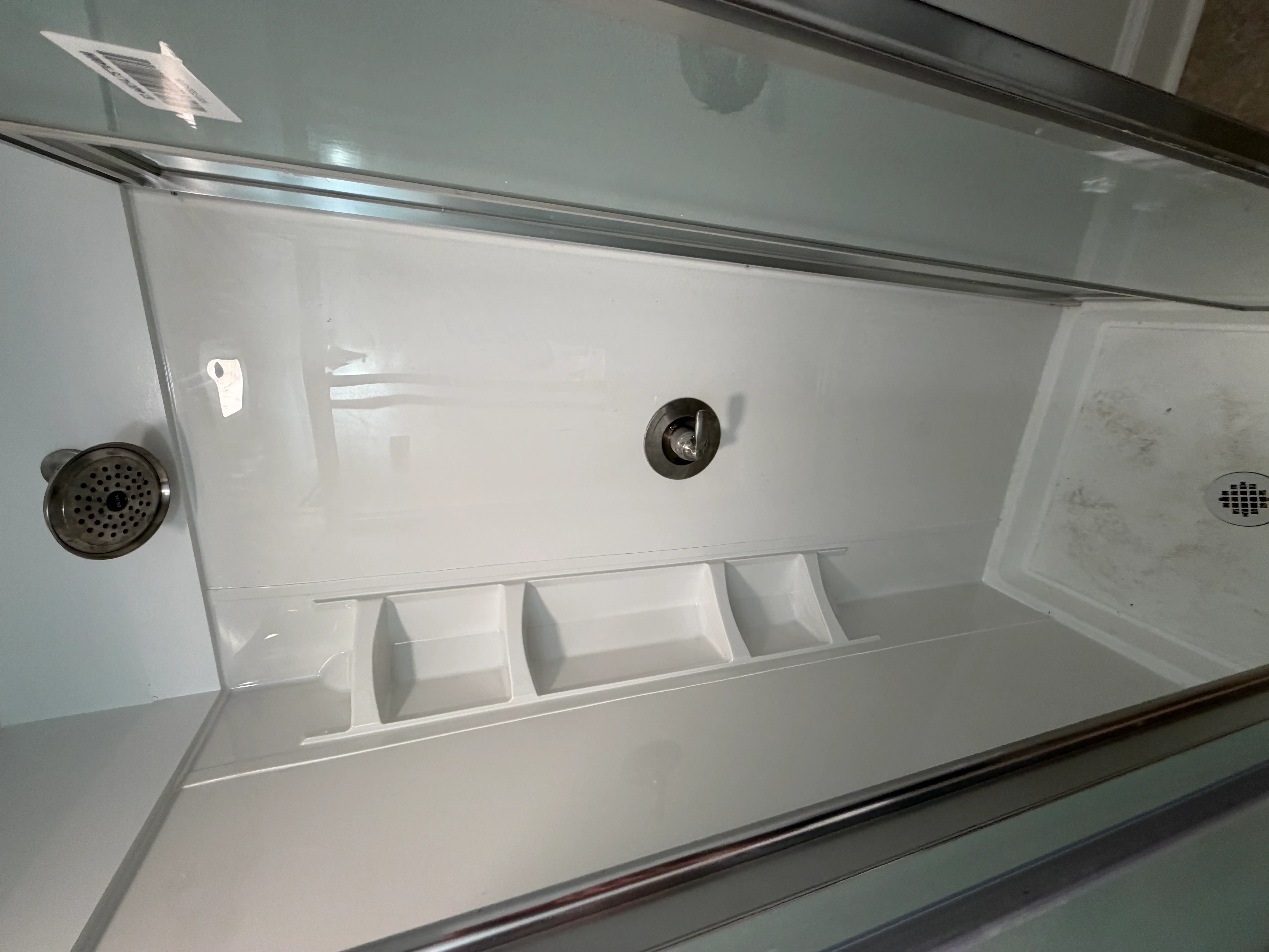 Frameless glass shower with chrome fixtures, body jets, and white acrylic walls with storage niche